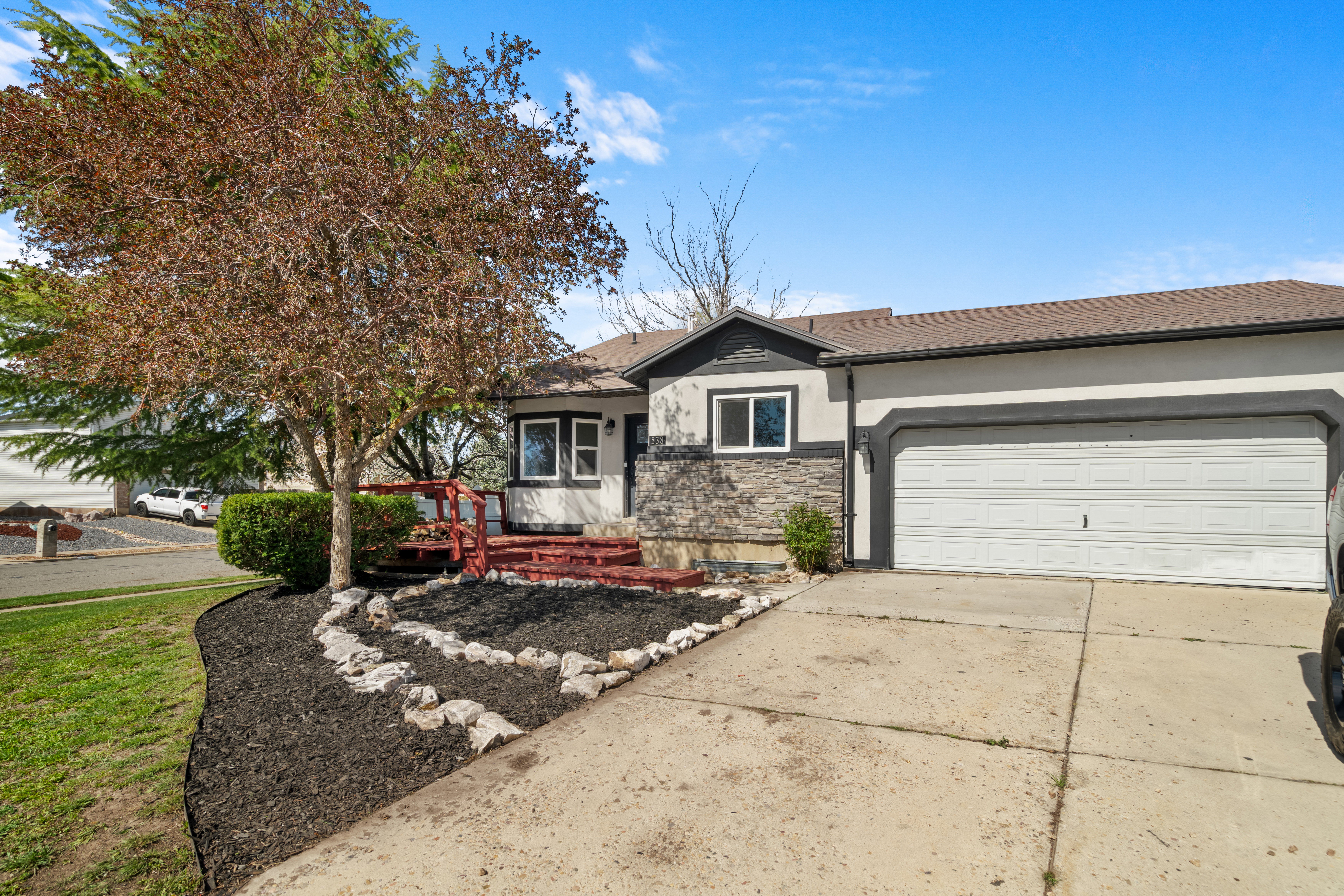 View of front of property featuring concrete driveway, stucco siding, a garage, stone siding, and a deck
