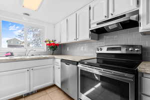 Kitchen with stainless steel appliances, tasteful backsplash, white cabinetry, light tile patterned floors, and a textured ceiling