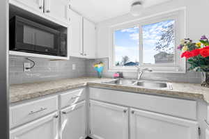 Kitchen featuring white cabinets, black microwave, light countertops, and tasteful backsplash