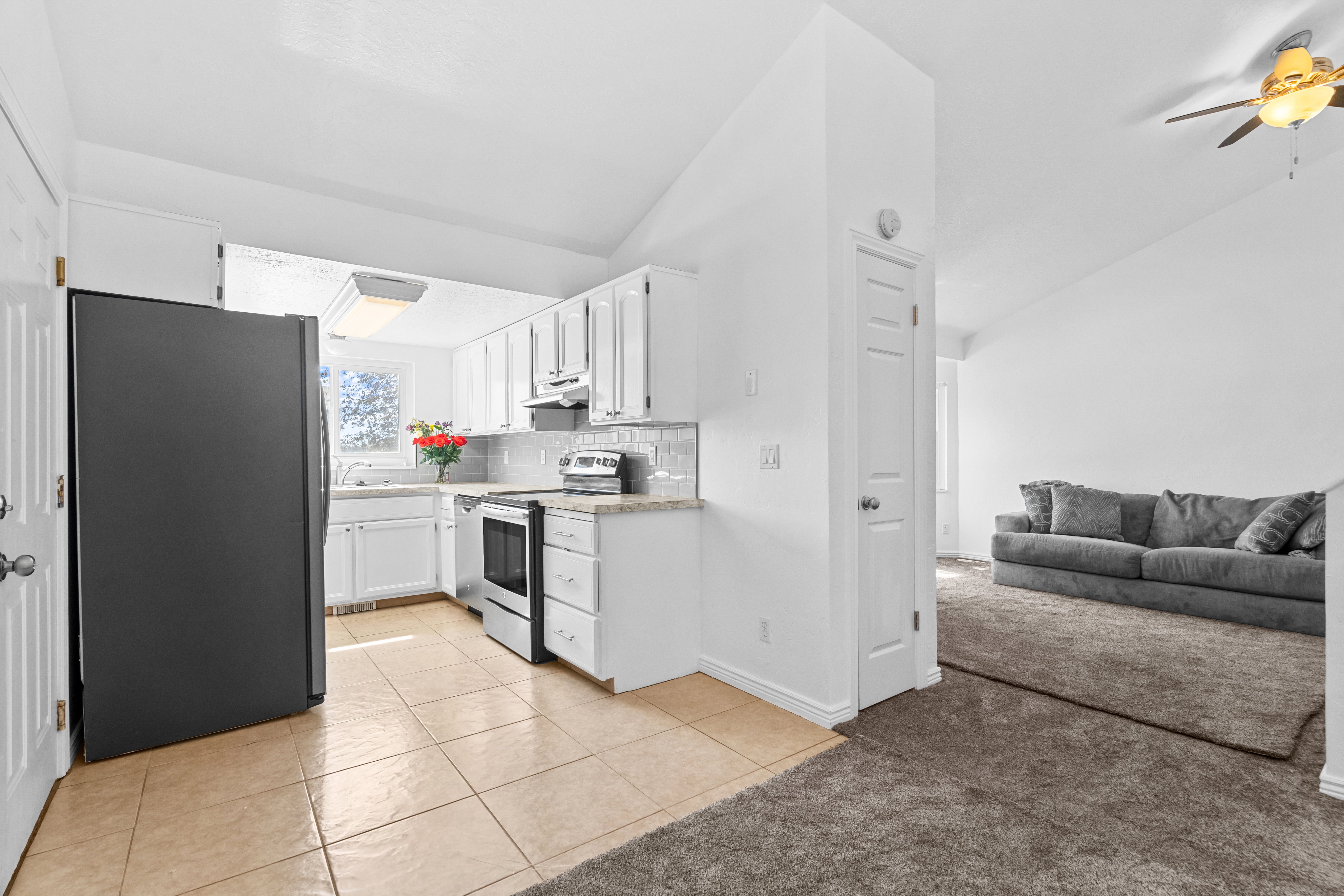 Kitchen with light tile patterned floors, stainless steel appliances, light countertops, light colored carpet, and white cabinetry