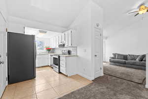 Kitchen with light tile patterned floors, stainless steel appliances, light countertops, light colored carpet, and white cabinetry