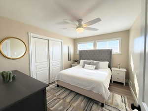 Bedroom with light LVP wood-style flooring, a ceiling fan, and a closet - enhanced photo staged.