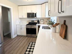 Kitchen featuring white cabinets, stainless steel appliances, light wood-style LVP flooring, and light stone countertops