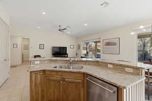 Kitchen featuring wood finish cabinets, a kitchen island with sink, dishwasher, open floor plan, and light stone counters