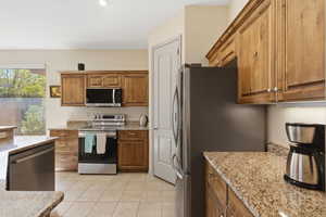 Kitchen featuring stainless steel appliances, light stone counters, wood finish cabinets, and light tile patterned flooring