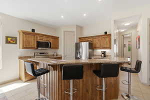 Kitchen featuring wood finish cabinets, a kitchen bar, light stone counters, light tile patterned floors, and recessed lighting
