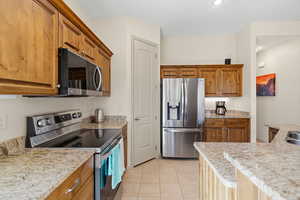 Kitchen featuring stainless steel appliances, light stone counters, wood finish cabinetry, and light tile patterned flooring