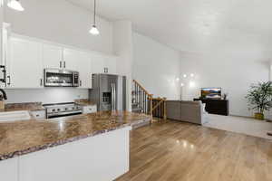 Kitchen with lofted ceiling, stainless steel appliances, open floor plan, white cabinetry, and dark countertops