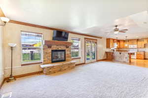 Unfurnished living room with light colored carpet, plenty of natural light, a stone fireplace, ceiling fan, and ornamental molding