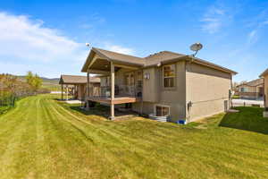 Rear view of house featuring a lawn, stucco siding, and a wooden deck