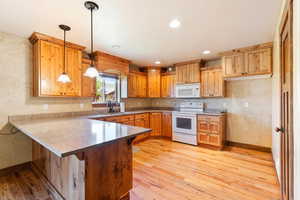 Kitchen with a peninsula, white appliances, a kitchen breakfast bar, light wood-type flooring, and a textured wall