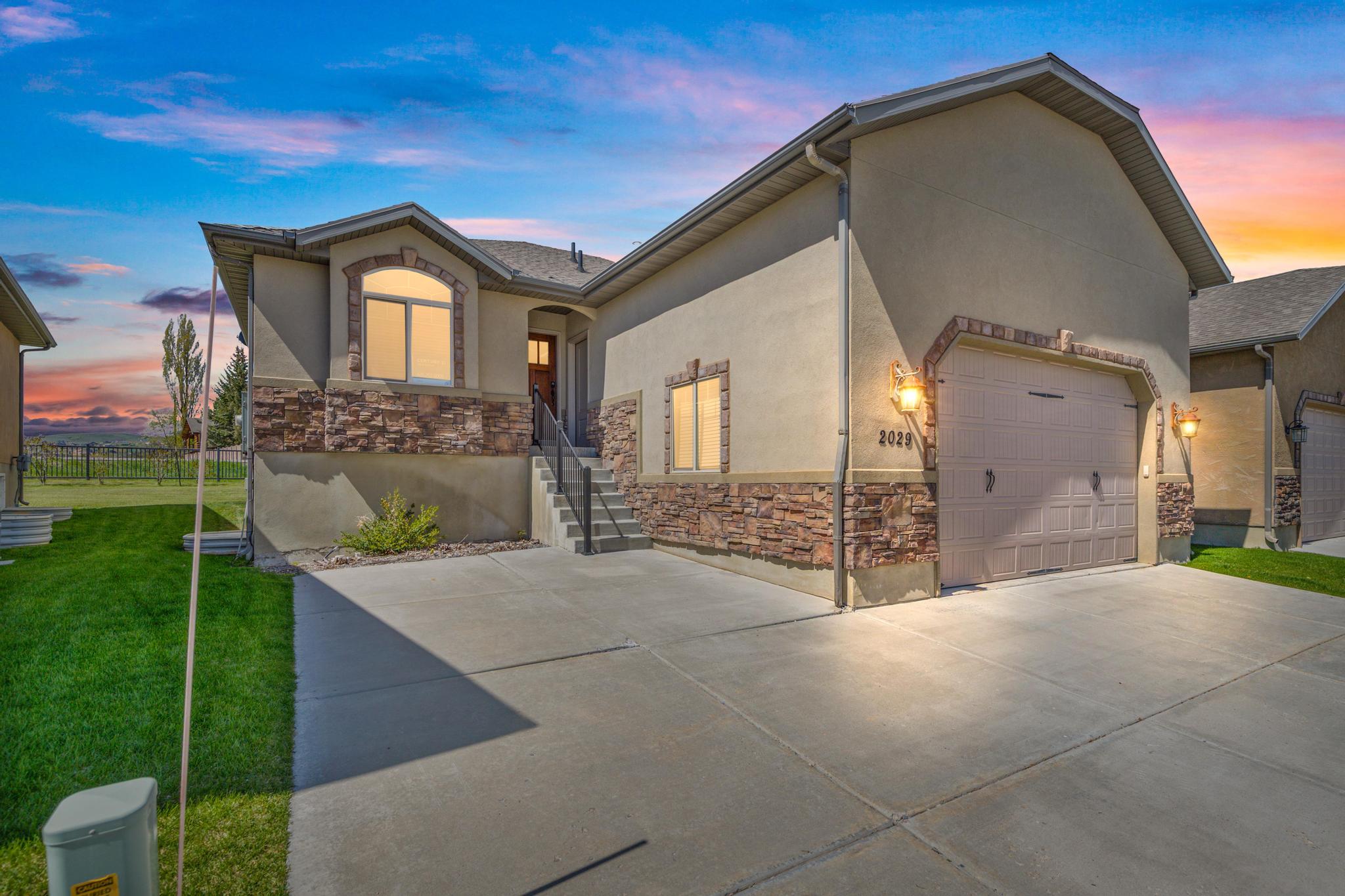 Ranch-style home with a garage, driveway, stone siding, and stucco siding