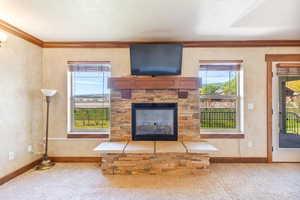 Unfurnished living room featuring ornamental molding, carpet floors, healthy amount of natural light, a stone fireplace, and a textured wall