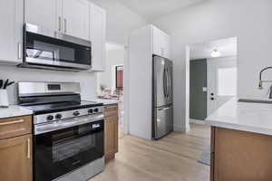 Kitchen with stainless steel appliances, light wood-style flooring, light stone counters, and white cabinets