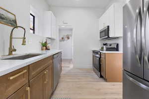 Kitchen with stainless steel appliances, two tone color scheme, light wood finished floors, and light stone counters