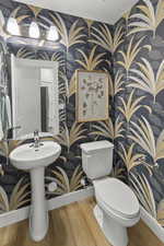 Half bath featuring wood finished floors and wallpapered walls