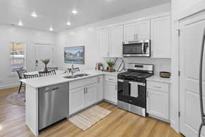 Kitchen with a peninsula, stainless steel appliances, white cabinets, light wood-style flooring, and recessed lighting