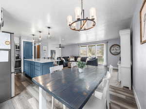 Dining area with dark wood-style flooring, ceiling fan, a chandelier, and a textured ceiling