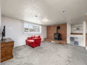 Living area featuring a wood stove, carpet floors, a textured ceiling, and wallpapered walls