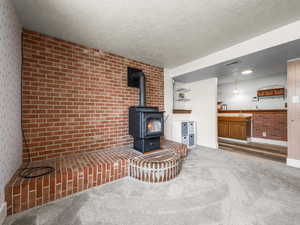Carpeted living area featuring brick wall, a textured ceiling, and a wood stove