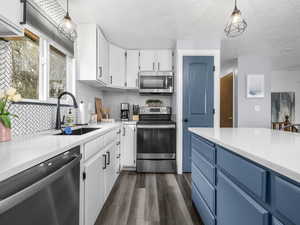 Dual tone kitchen with two tone color scheme, stainless steel appliances, pendant lighting, dark wood-style floors, and light stone countertops