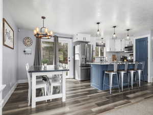 Two tone kitchen with a kitchen breakfast bar, stainless steel appliances, dual tone cabinetry, suspended lighting, and dark wood-style flooring
