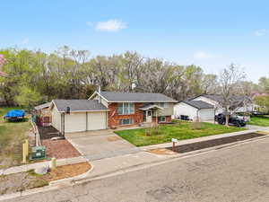 Bi-level home featuring brick siding, driveway, a garage, a front lawn, and a shingled roof