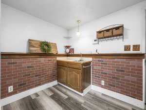 Indoor wet bar featuring dark wood-style floors, brick wall, light countertops, hanging light fixtures, and wood finish cabinetry