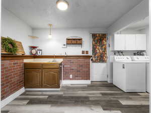 Laundry area featuring cabinet space, dark wood-type flooring, washer and dryer, a textured ceiling, and bar with sink
