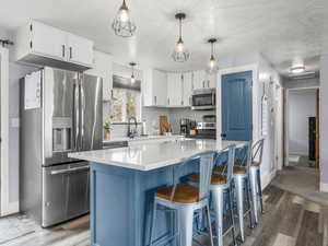 Two tone kitchen with stainless steel appliances, a kitchen island, a kitchen bar, a textured ceiling, and dark wood-style flooring