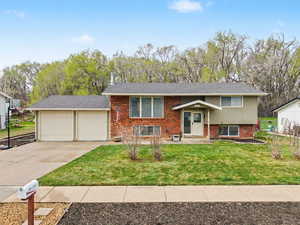 Raised ranch featuring brick siding, a garage, driveway, and a front yard