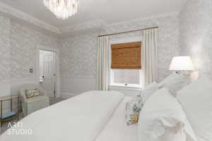 Bedroom featuring crown molding, hanging lights, and a wainscoted wall