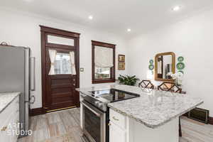 Kitchen featuring stainless steel appliances, light stone countertops, white cabinetry, a kitchen island, and ornamental molding
