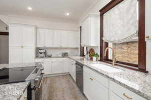 Kitchen featuring stainless steel appliances, light wood finished floors, white cabinets, light stone counters, and crown molding