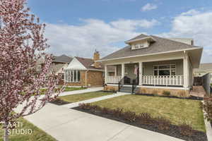 Bungalow-style home with roof with shingles, a porch, a front yard, and brick siding