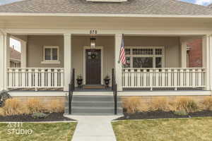 Entrance to property with a shingled roof, a porch, and brick siding
