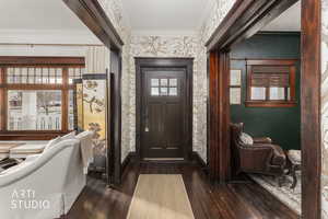 Entryway featuring dark wood-type flooring, ornamental molding, plenty of natural light, and wallpapered walls
