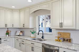 Kitchen with light stone counters, stainless steel dishwasher, tasteful backsplash, cream cabinets, and recessed lighting