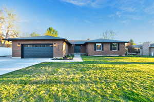 Single story home featuring brick siding, driveway, a front lawn, and a garage