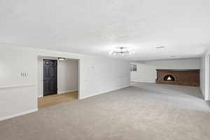 Unfurnished living room with light carpet, a fireplace, and a textured ceiling