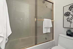 Full bath featuring toilet and combined bath / shower with glass door