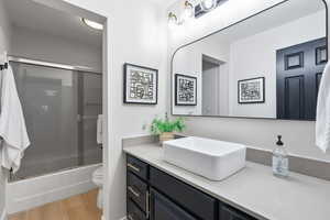 Bathroom with vanity, enclosed tub / shower combo, and light wood-style flooring