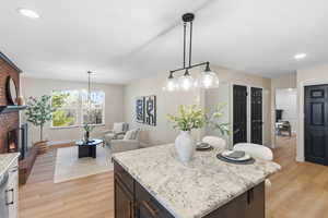 Kitchen with light wood-type flooring, light stone countertops, a kitchen island, and a brick fireplace