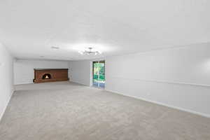 Unfurnished living room featuring a fireplace, light colored carpet, and a textured ceiling