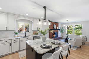 Two tone kitchen featuring decorative backsplash, a kitchen island, light wood-type flooring, light stone counters, and a breakfast bar area