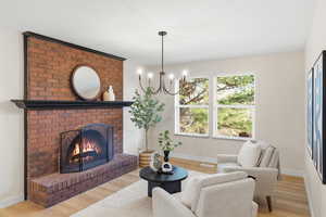 Living room with light wood finished floors, a brick fireplace, and suspended lighting