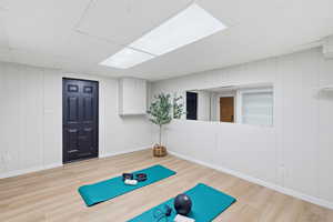 Workout area with light wood finished floors, a paneled ceiling, and wooden walls