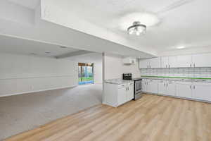 Kitchen with electric stove, white cabinetry, decorative backsplash, light colored carpet, and light wood-type flooring