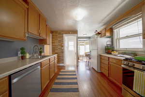Kitchen featuring stainless steel appliances, light countertops, a textured ceiling, and dark wood-type flooring
