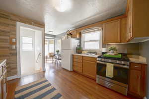 Kitchen featuring stainless steel gas range, light countertops, freestanding refrigerator, light wood-style floors, and a textured ceiling